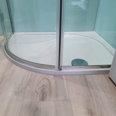 Bottom of a corner, curved shower cubicle, grey flooring and turquoise backsplash