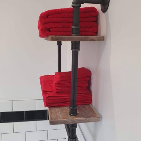 Industrial type bathroom shelving, black pipes, 2 dark wood shelves with red towels folded on the shelves