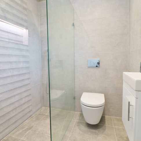 Wetroom with modern, white sink unit and toilet. Glass panel separates the shower unit on the right