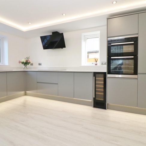 White and grey kitchen, white wall, grey units, with led lights at plinth level